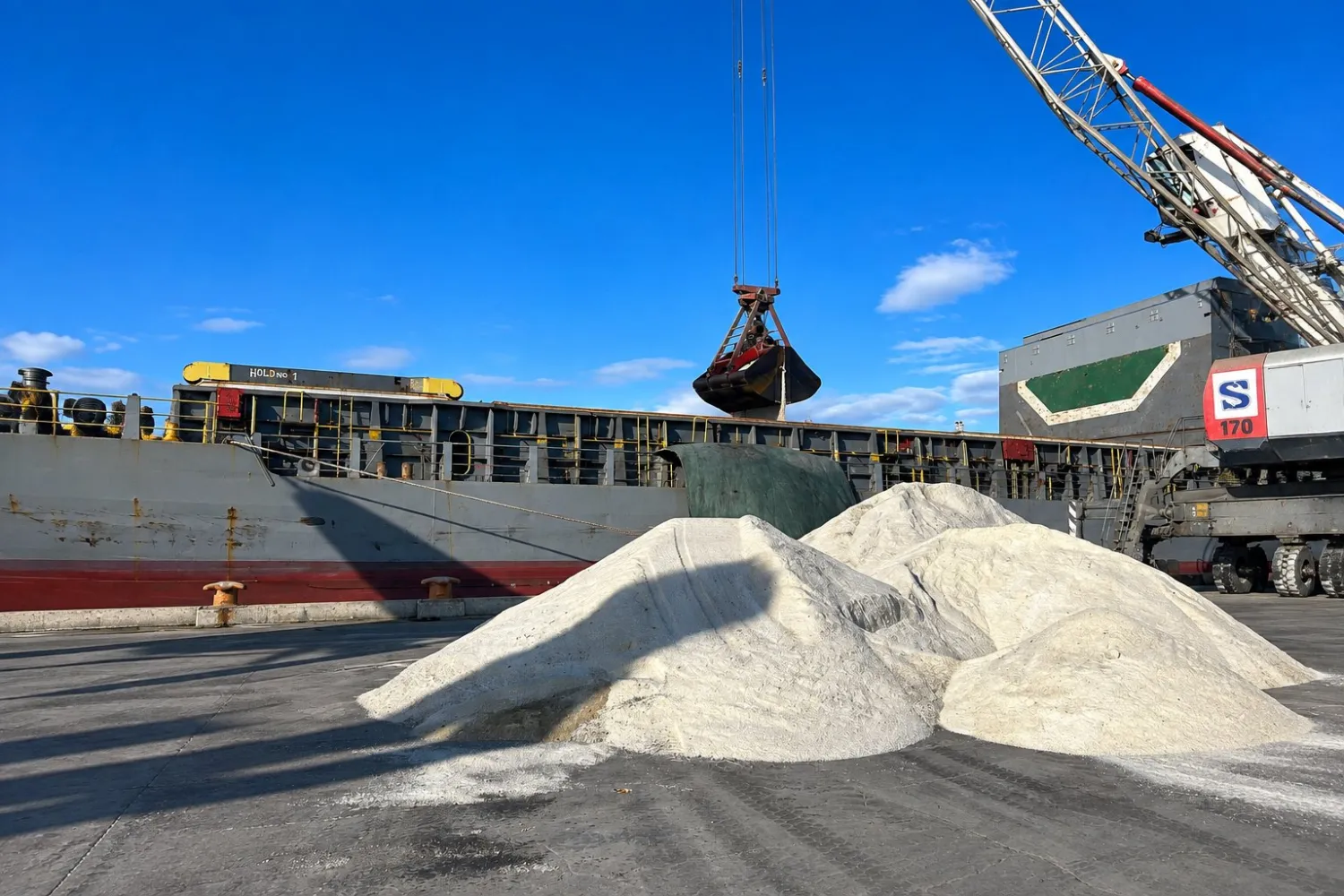Grab discharging white dry bulk cargo onto a quay stockpile next to a bulk carrier