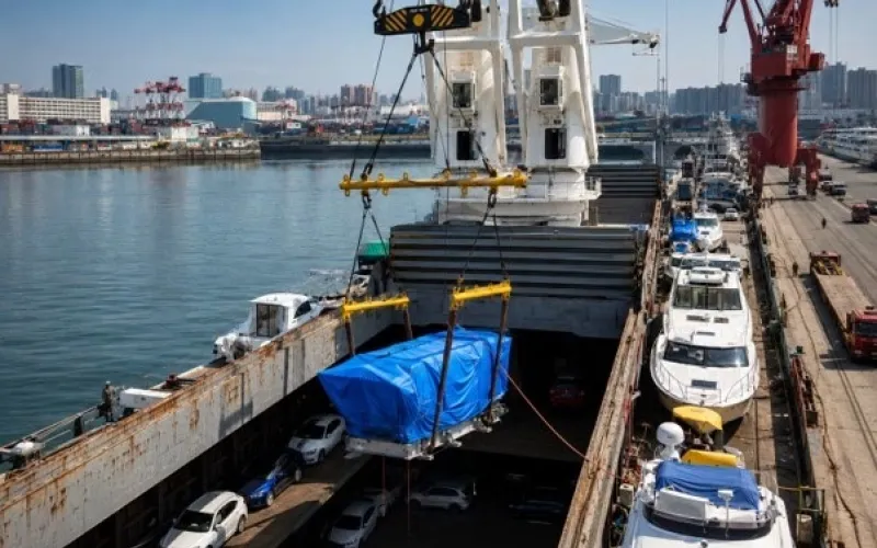 Ship's crane lifting a covered heavy unit into a cargo hold with cars and yachts — Construction Review Online article by Konstantin Kalnyi
